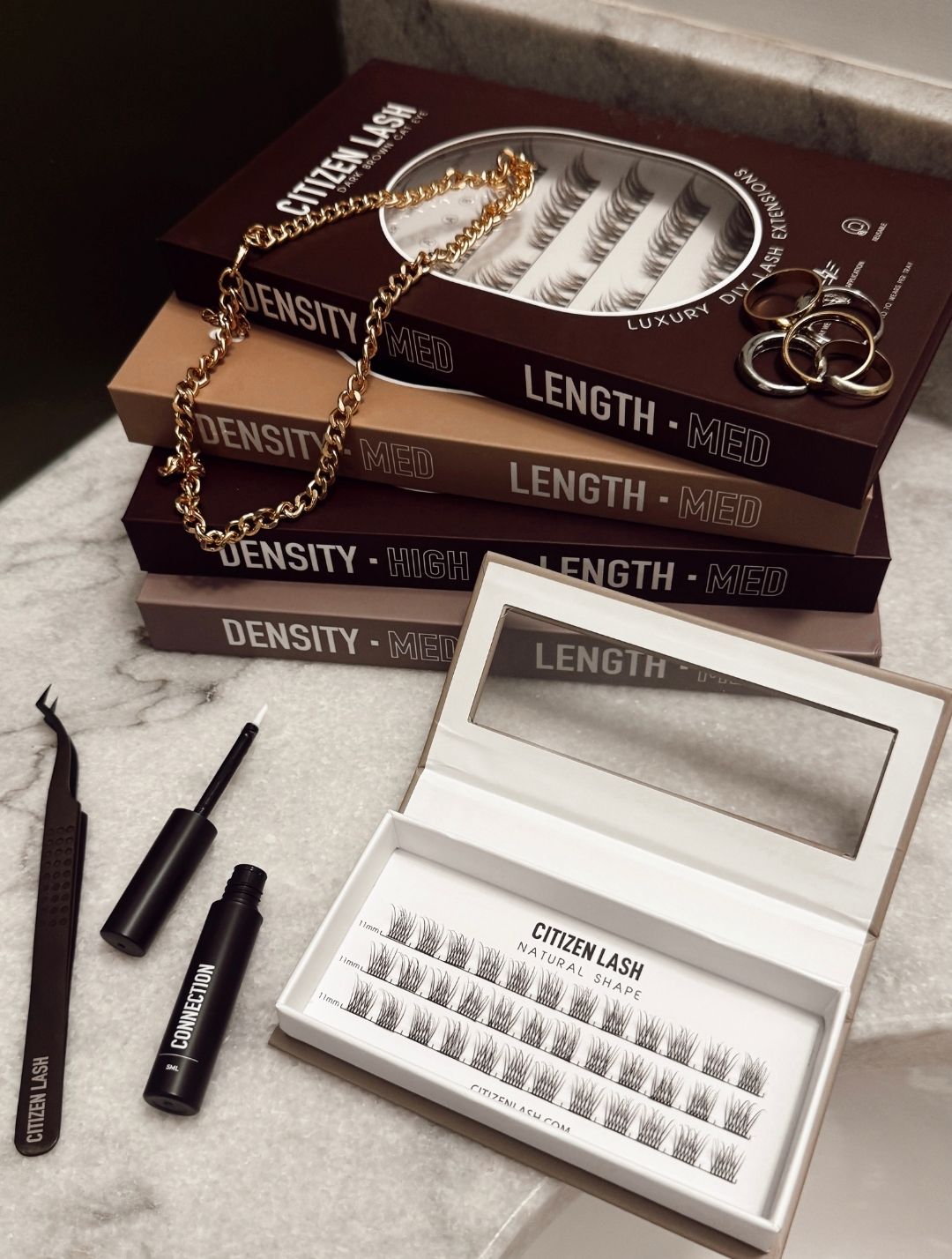 Eyelash extension kit with open box, lashes, and tools on a marble surface.