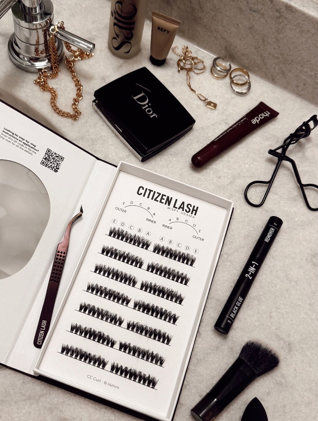 Eyelash extension kit with tools and Dior product on a counter